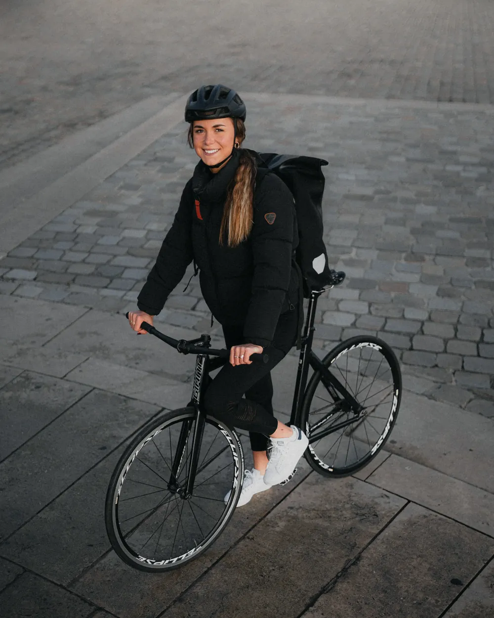 Livreuse Blackbird souriante avec son vélo sur les pavés